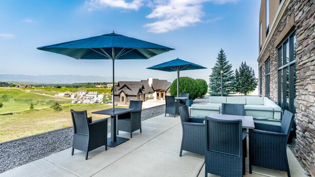 Eine Terrasse im Freien mit Korbmöbeln und blauen Sonnenschirmen, mit Blick auf eine schöne Landschaft.