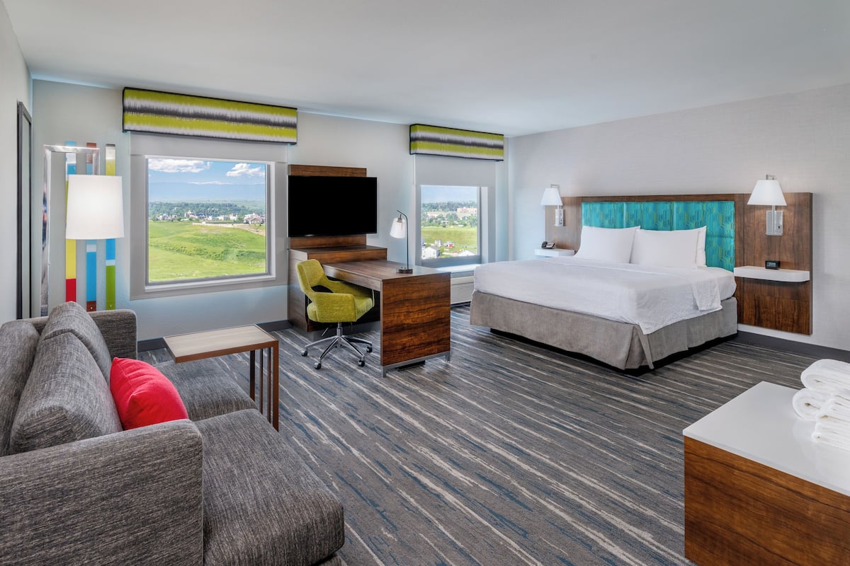 Quarto de hotel com cama, escrivaninha, televisão e vista para o exterior.