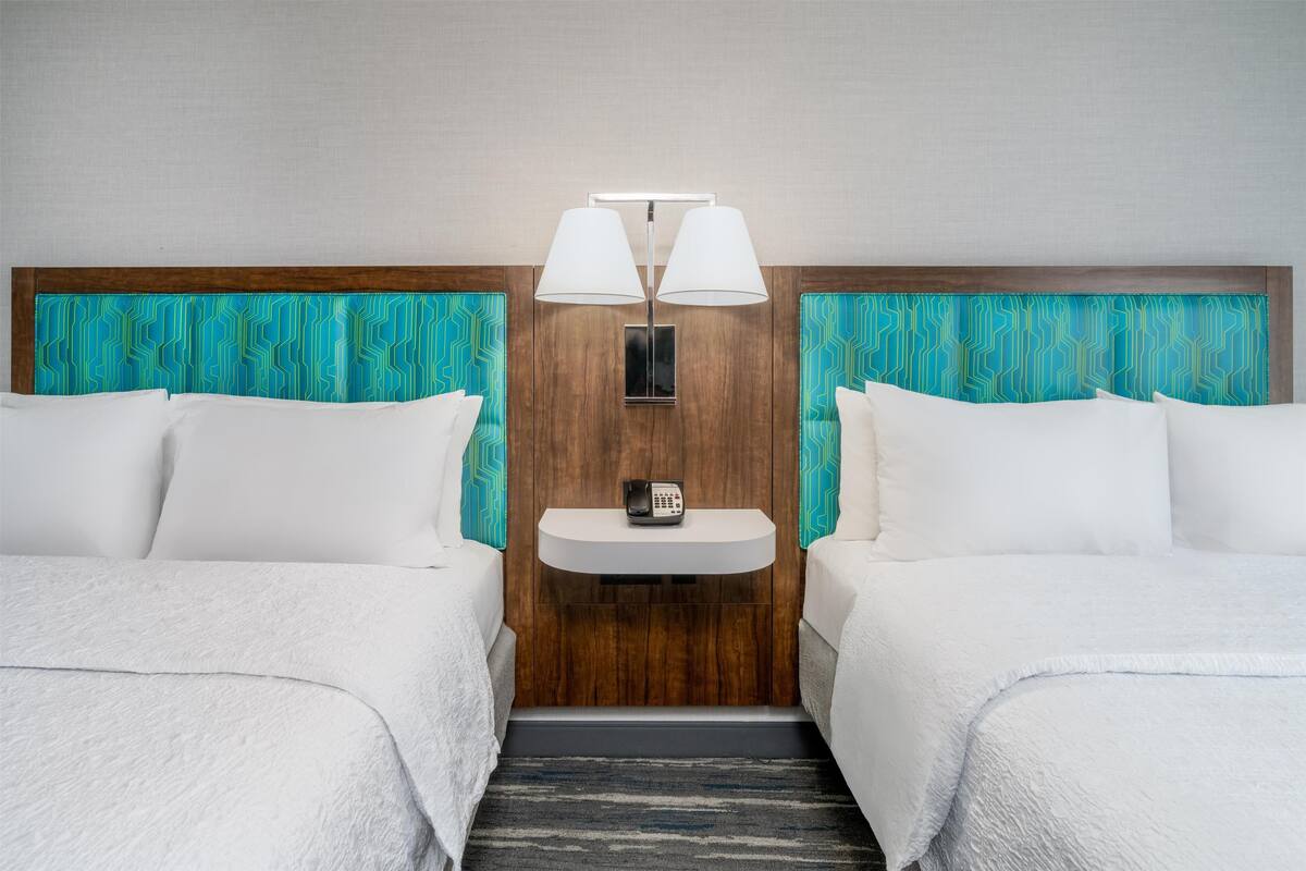 Quarto de hotel com duas camas, uma mesa de cabeceira com telefone e uma luminária na parede.