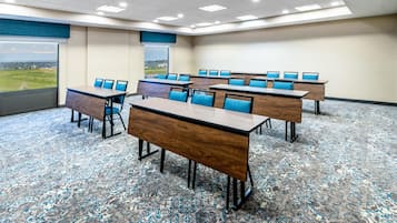A conference room with multiple tables and chairs, carpeted floor, and large windows offering a view.