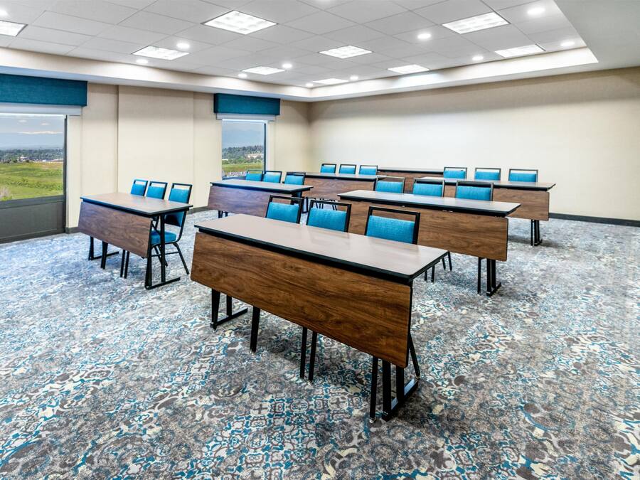 A conference room with multiple tables and chairs, carpeted floor, and large windows offering a view.