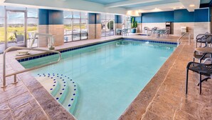 Ein Innenpool mit klarem, blauem Wasser, umgeben von Steinfliesen und blauen Wänden. Am Poolufer befinden sich Liegestühle und Tische.