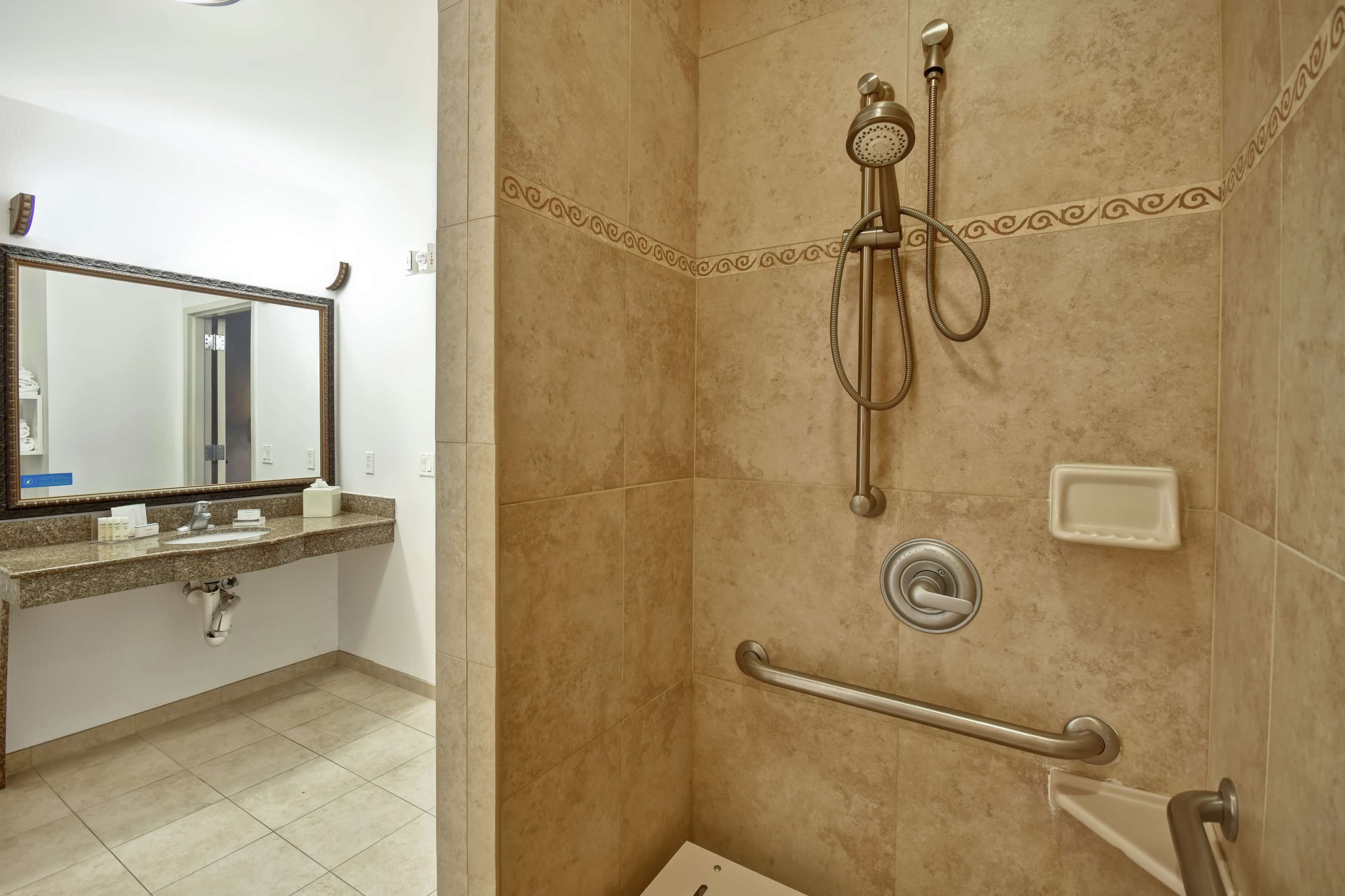 Un baño con ducha, lavamanos, espejo y barandilla.