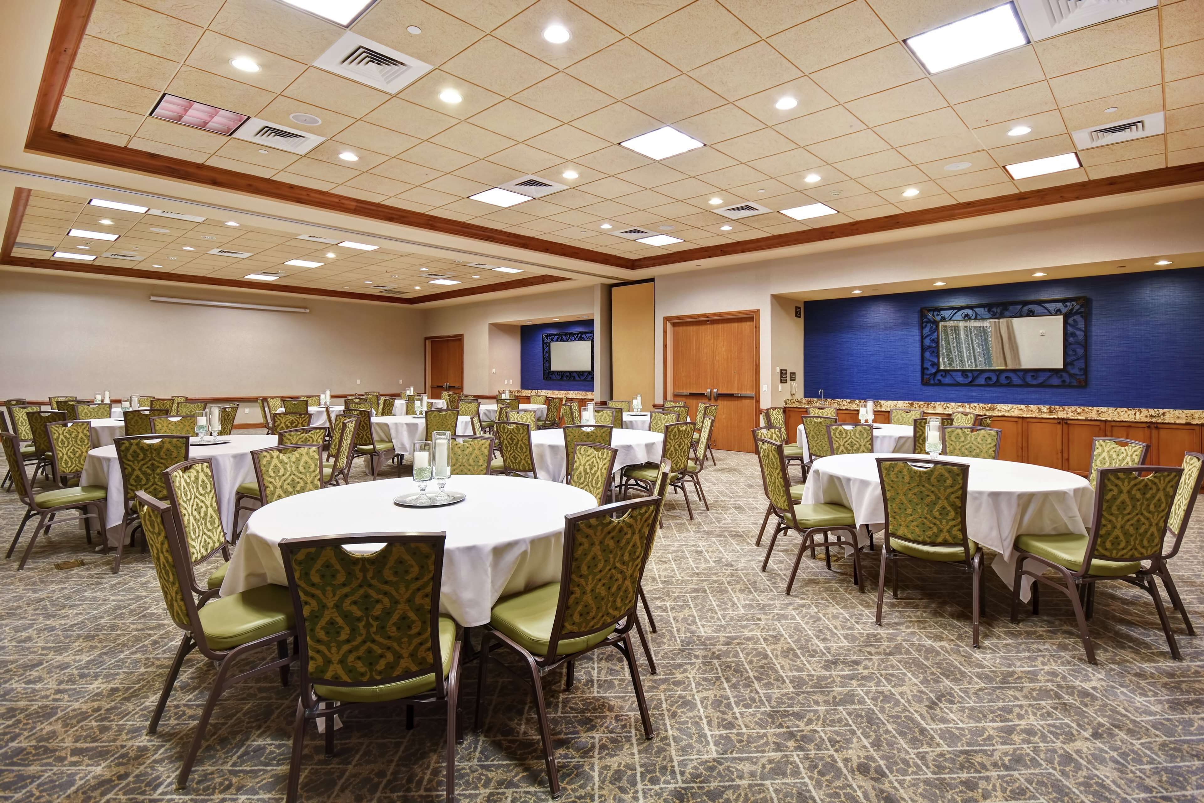 A conference room with multiple round tables, green upholstered chairs, and a patterned carpet.