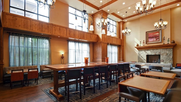 A spacious room with a long wooden table and multiple chairs, a fireplace, and large windows allowing natural light. - Hampton Inn & Suites Salt Lake City-West Jordan (West Jordan)