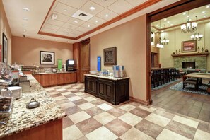 A hotel lobby with a checkered floor, a reception desk, a fireplace, and a dining area.