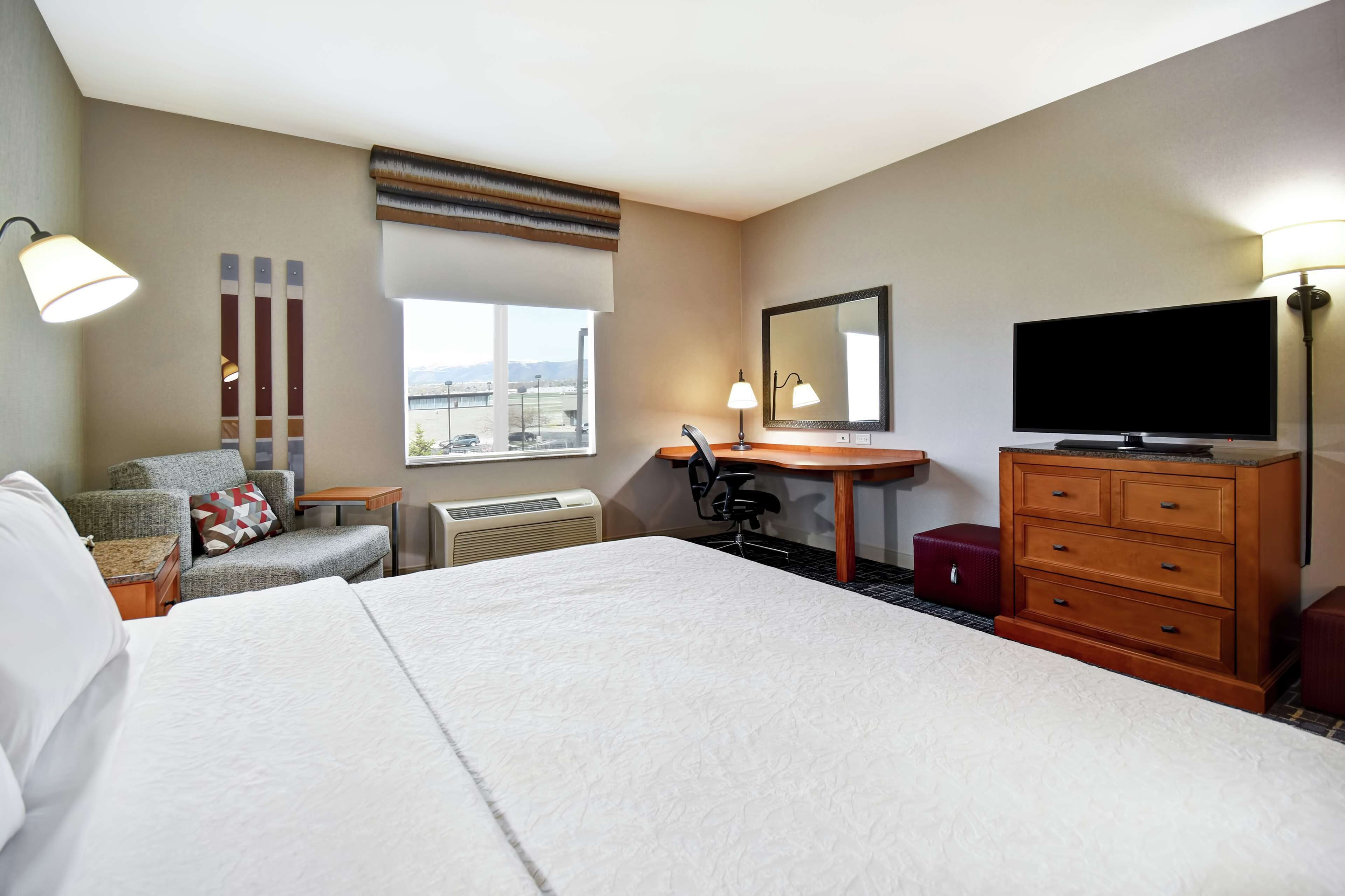 Quarto de hotel com uma cama grande, uma escrivaninha com cadeira, uma televisão e uma janela com vista para a cidade.