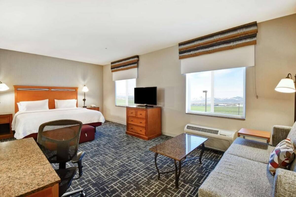 Habitación de hotel con cama, televisión, escritorio, silla, sofá y ventana con vista.
