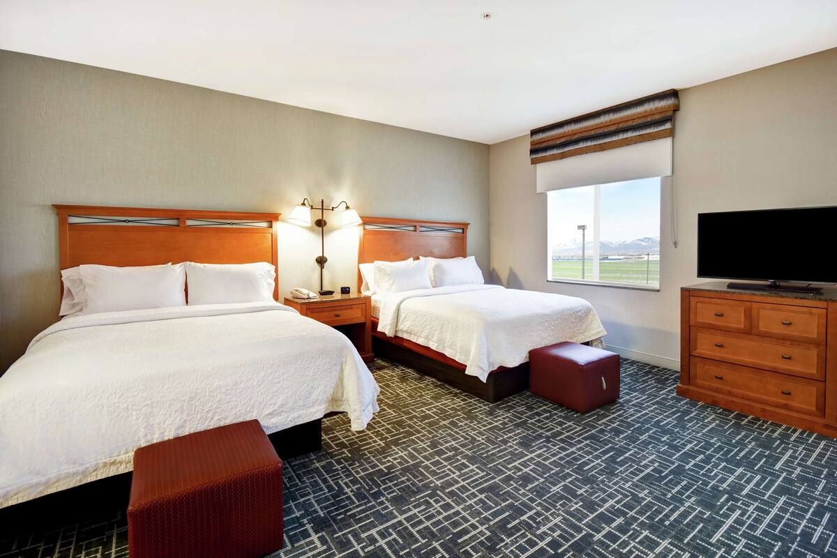 Habitación de hotel con dos camas, televisión, cómoda y ventana con vistas.
