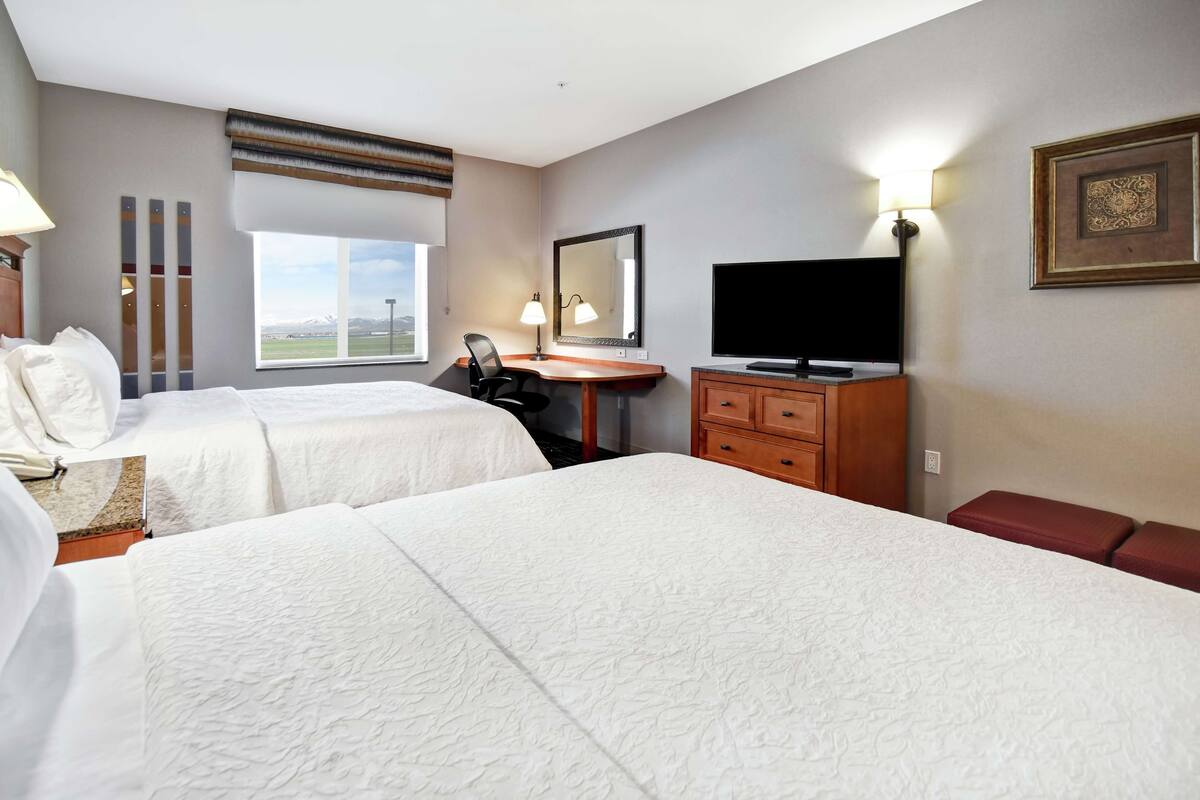 Habitación de hotel con dos camas, un escritorio, televisión y ventana con vistas a las montañas.