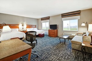 Quarto de hotel com duas camas, uma escrivaninha, uma cadeira, uma televisão e vista para as montanhas.