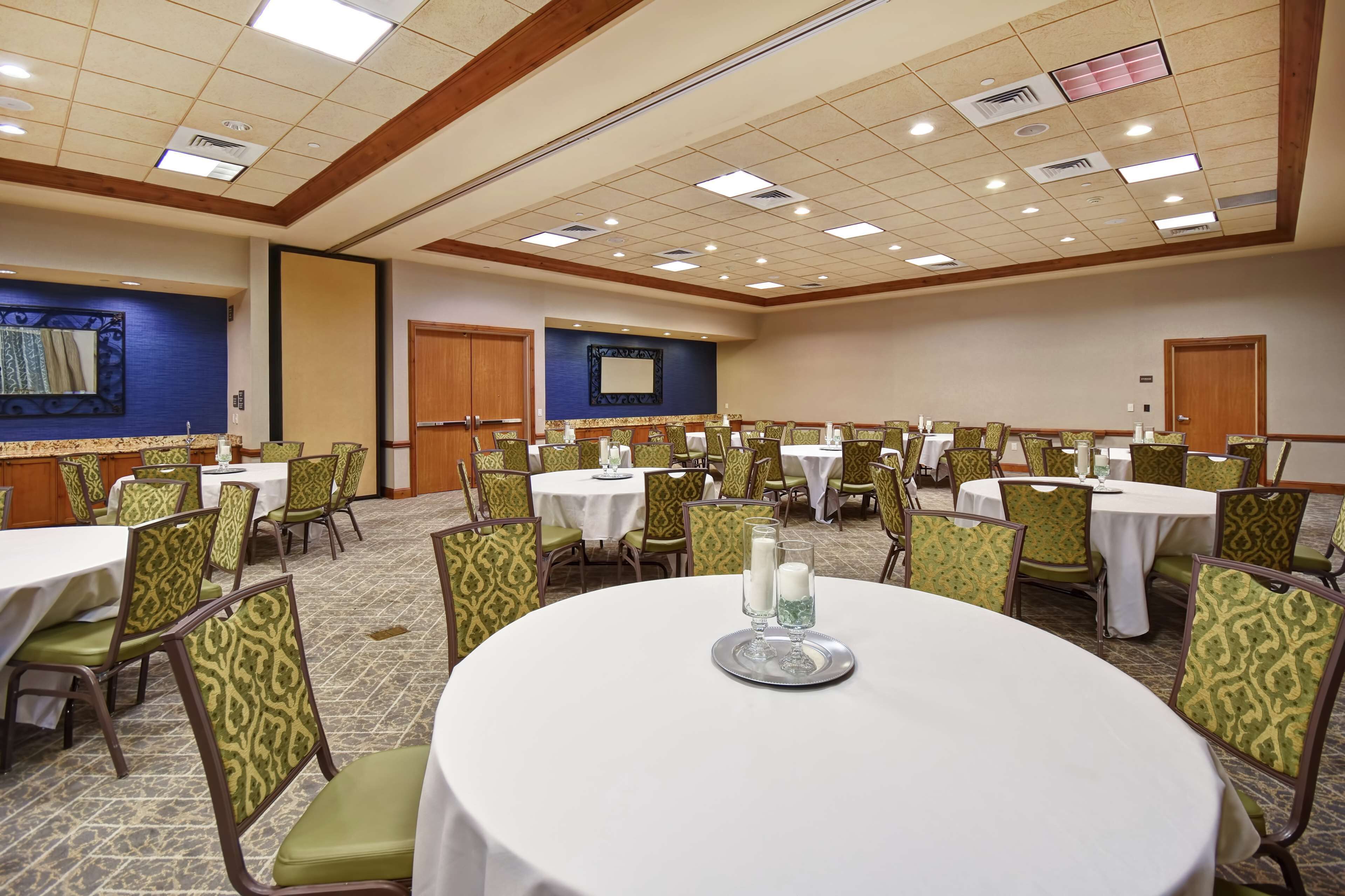 A conference room with round tables and green patterned chairs, featuring a carpeted floor and a blue accent wall.