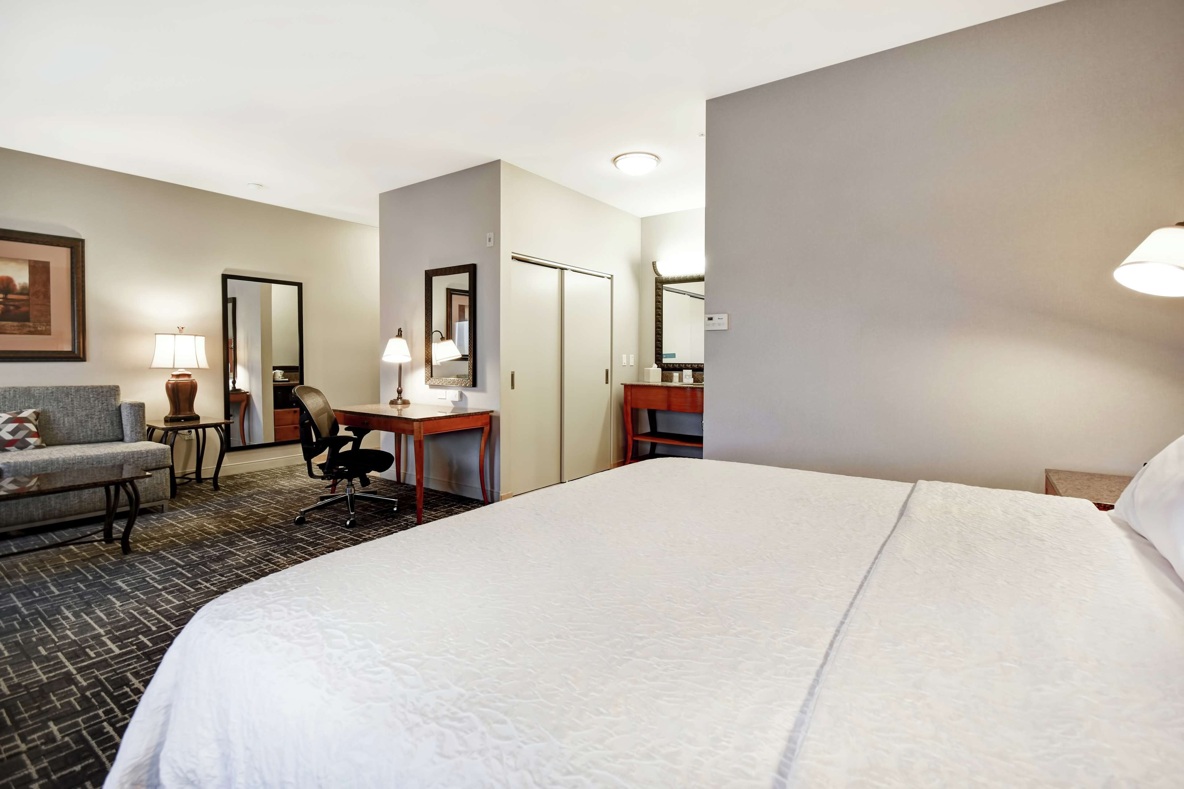 A hotel room with a large bed, a desk with a chair, a sofa, and a small table with a lamp.