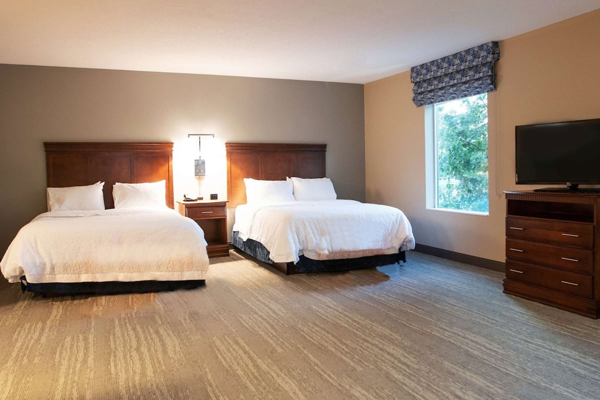 A hotel room with two beds, a nightstand with a lamp, a dresser, and a TV.