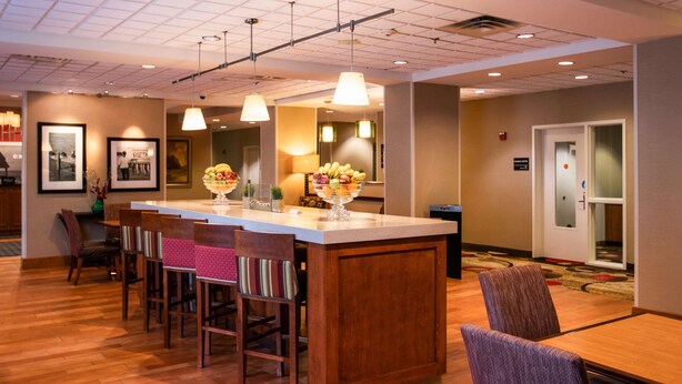 A hotel lobby with a reception desk, chairs, a fruit bowl, framed pictures, and a waste bin. - Hampton Inn Gloucester (Gloucester)