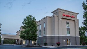 A Hampton Inn hotel with a modern facade, large windows, and a well-maintained lawn.