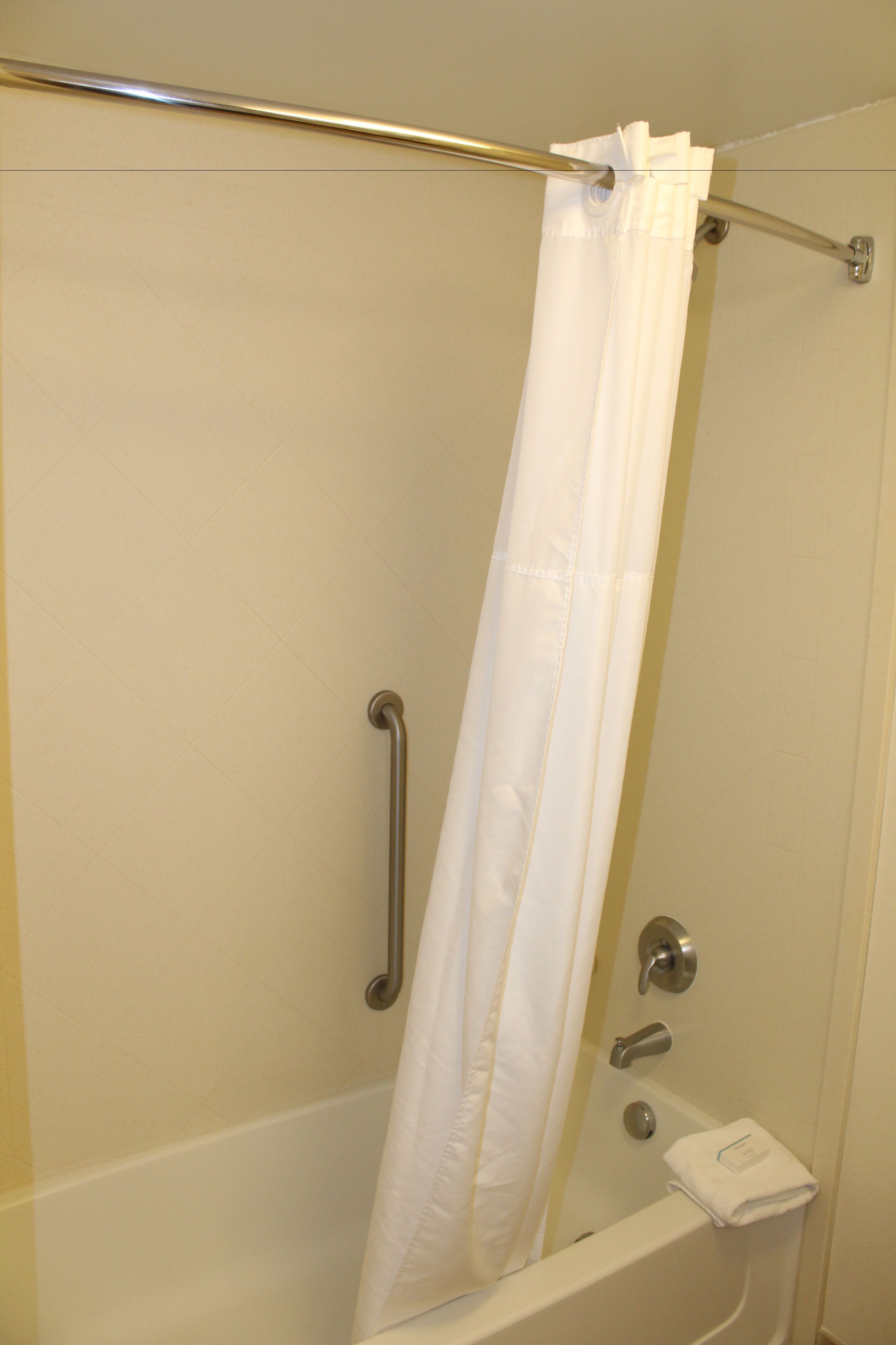 Une douche avec un rideau blanc, une barre d’appui et un porte-serviettes.