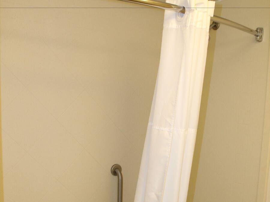 A shower with a white curtain, a grab bar, and a towel rack.