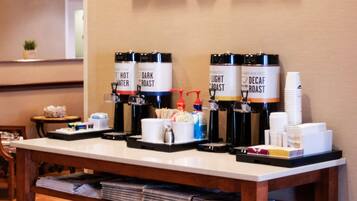 Een koffiehoek met dispensers met etiketten voor heet water, donkere branding, lichte branding en decaf koffie.