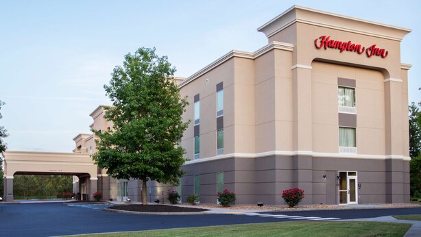 A Hampton Inn hotel building with a beige facade, large windows, and a clear sky.
