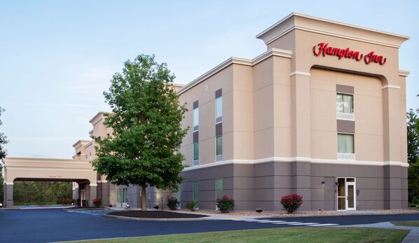 A Hampton Inn hotel building with a beige facade, large windows, and a clear sky.