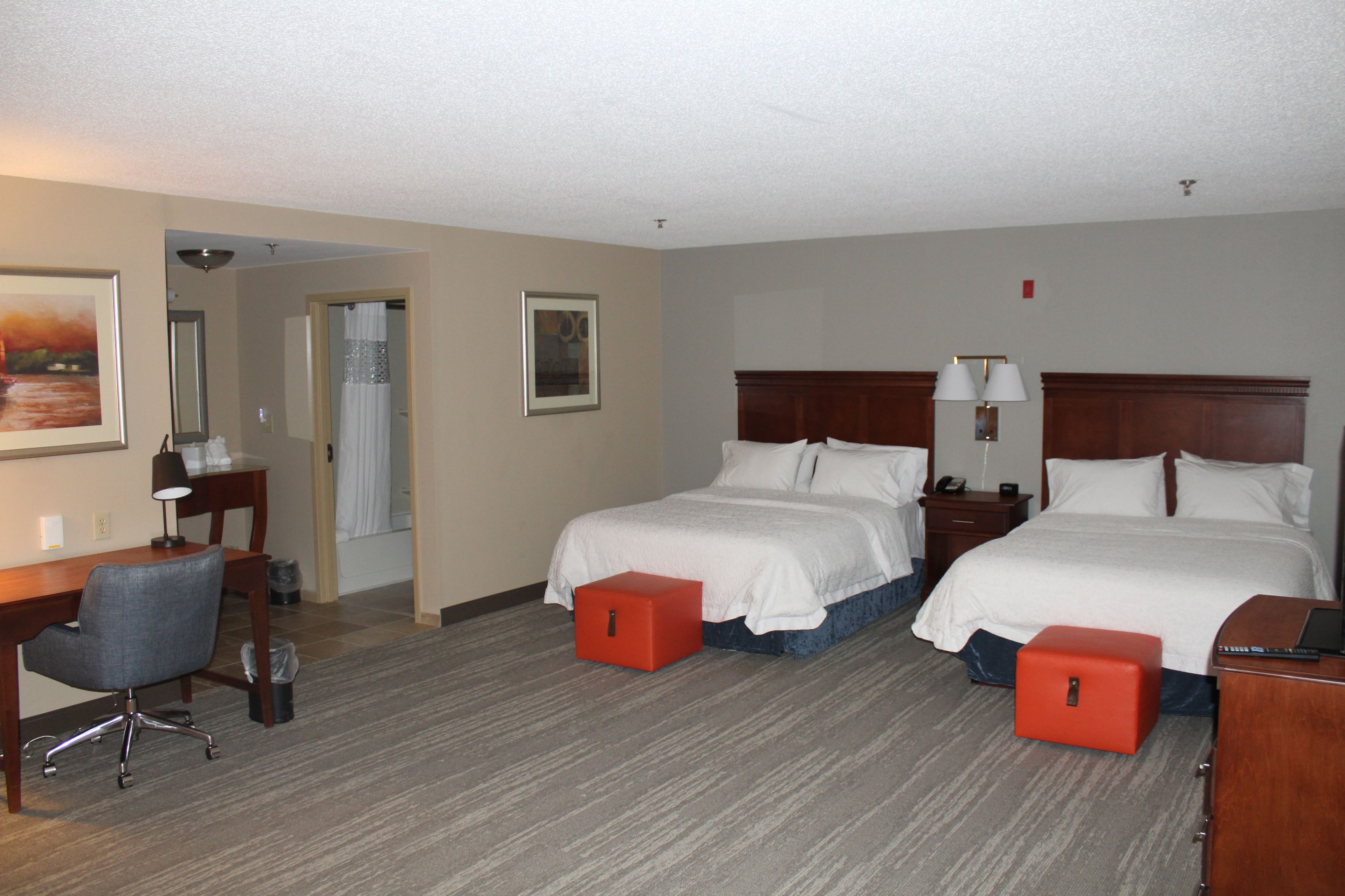 A hotel room with two beds, a desk, a chair, and a small table.
