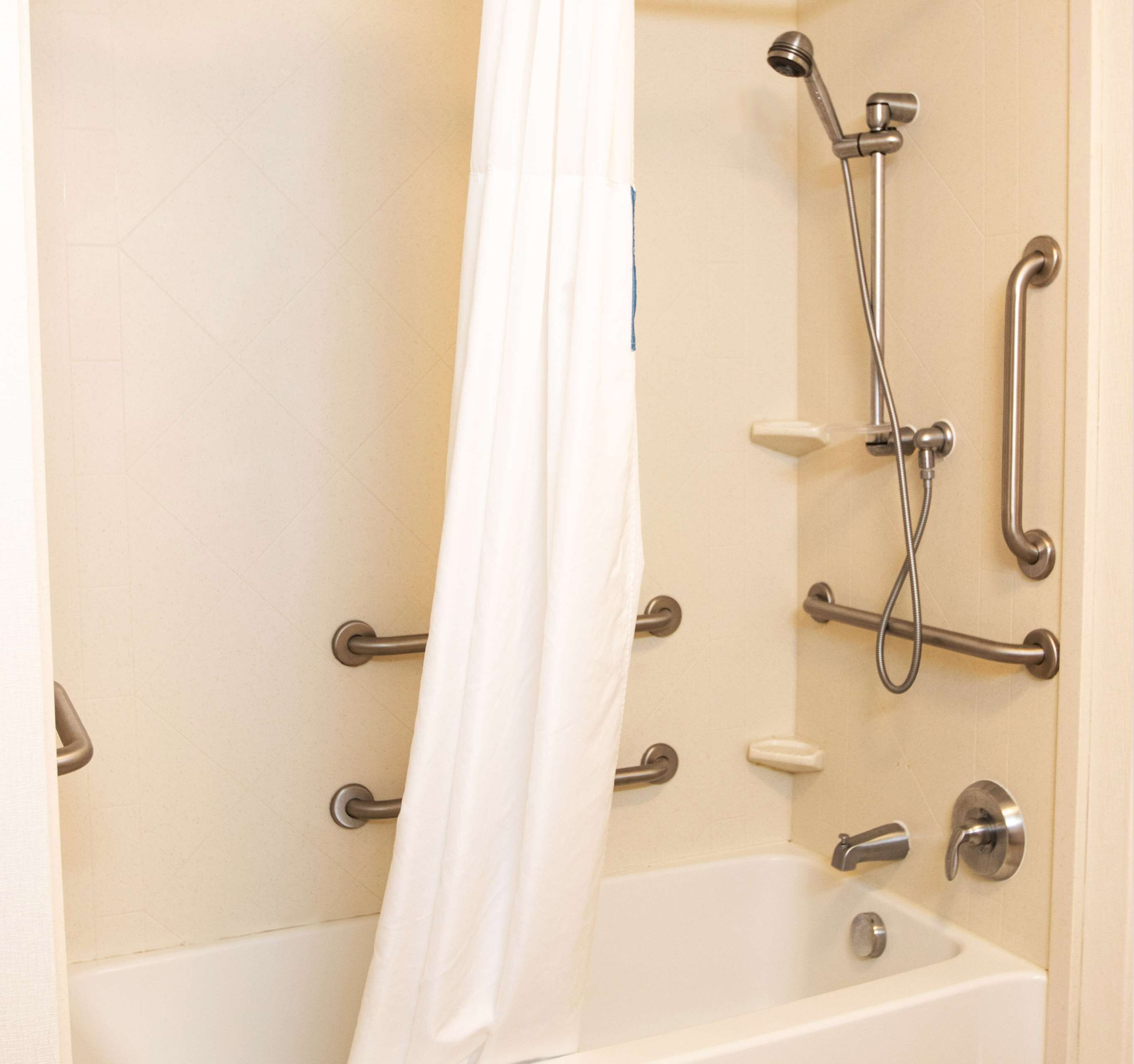 A bathroom with a bathtub, shower, and grab bars.