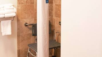 A bathroom with a shower, grab bars, a wheelchair-accessible bench, and a towel rack with folded towels.