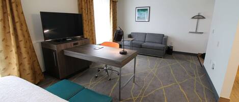 A hotel room with a bed, a desk with a television, a sofa, and a patterned carpet.