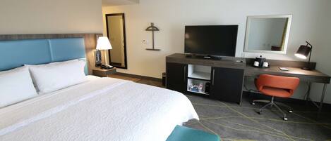 Una habitación de hotel con cama, escritorio, silla, televisor y espejo.