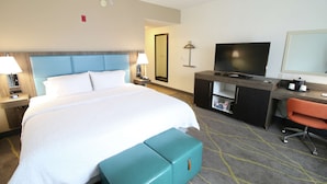 A hotel room with a large bed, a desk with a TV, a chair, and a small cabinet. - Hampton Inn & Suites Palm Coast (Palm Coast)