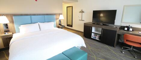A hotel room with a large bed, a desk with a TV, a chair, and a small cabinet.