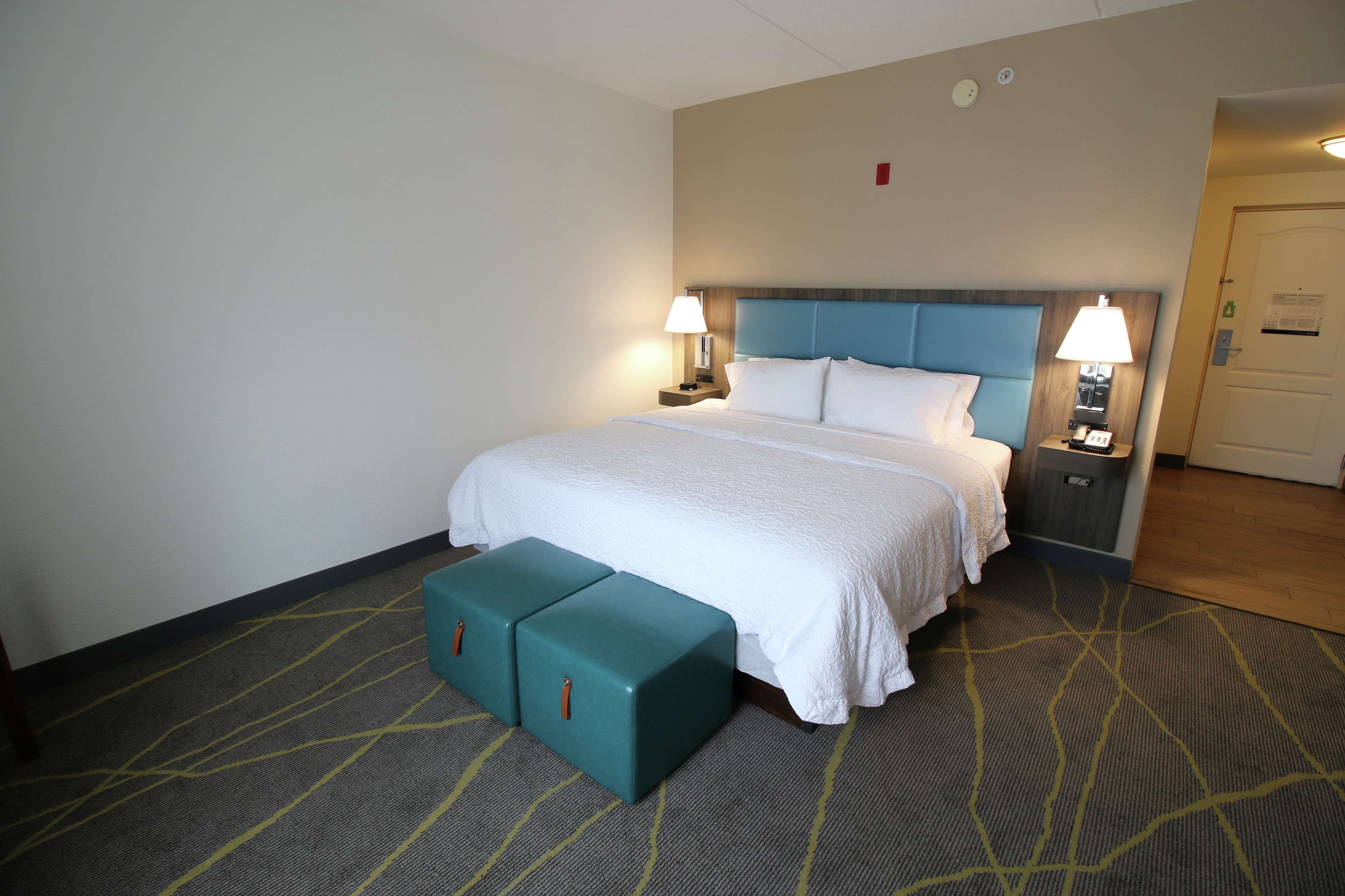 A hotel room with a bed, two bedside tables, a nightstand, and a bench.