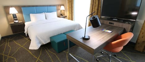 Habitación de hotel con cama, escritorio, silla, televisor y lámpara.