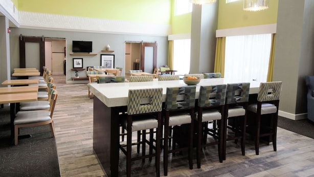 A spacious dining area with a long table and multiple chairs, a television mounted on the wall, and a large window providing natural light. - Hampton Inn & Suites Palm Coast (Palm Coast)
