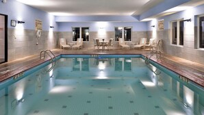 A swimming pool with lounge chairs and a table, surrounded by tiled walls and windows. - Hampton Inn Kansas City Northeast (Kansas City)