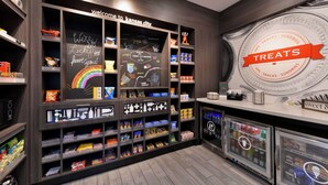 A snack and sundries display area with shelves stocked with various snacks and a chalkboard wall with a welcome message. - Hampton Inn Kansas City Northeast (Kansas City)