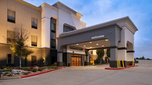 A hotel entrance with a 'welcome' sign, a covered driveway, and a landscaped area with rocks and plants. - Hampton Inn Kansas City Northeast (Kansas City)