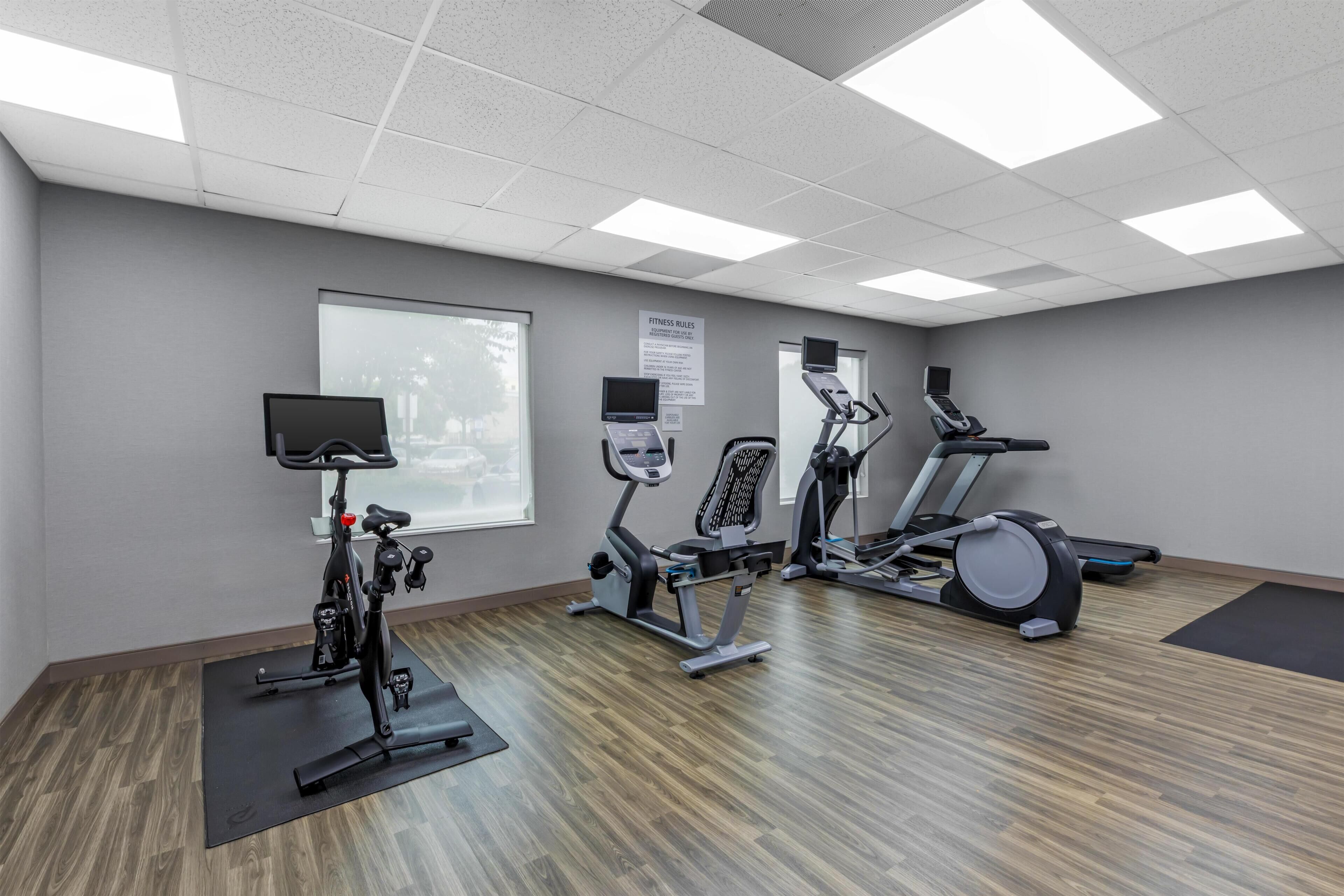 A fitness room with exercise equipment, a large window, and a sign detailing equipment rules.
