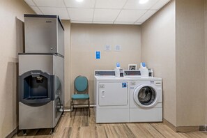 A laundry room with a commercial washer and dryer, a water fountain, and a chair. - Hampton Inn & Suites Atlanta Airport West/Camp Creek Pkwy (Atlanta)