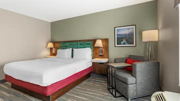 A hotel room with a bed, a desk, a chair, a nightstand, a lamp, and a painting on the wall.
