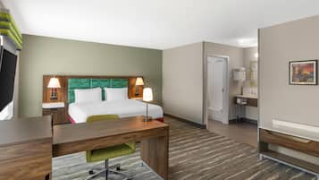 Quarto de hotel com cama, escrivaninha, cadeira e banheiro com pia e espelho.