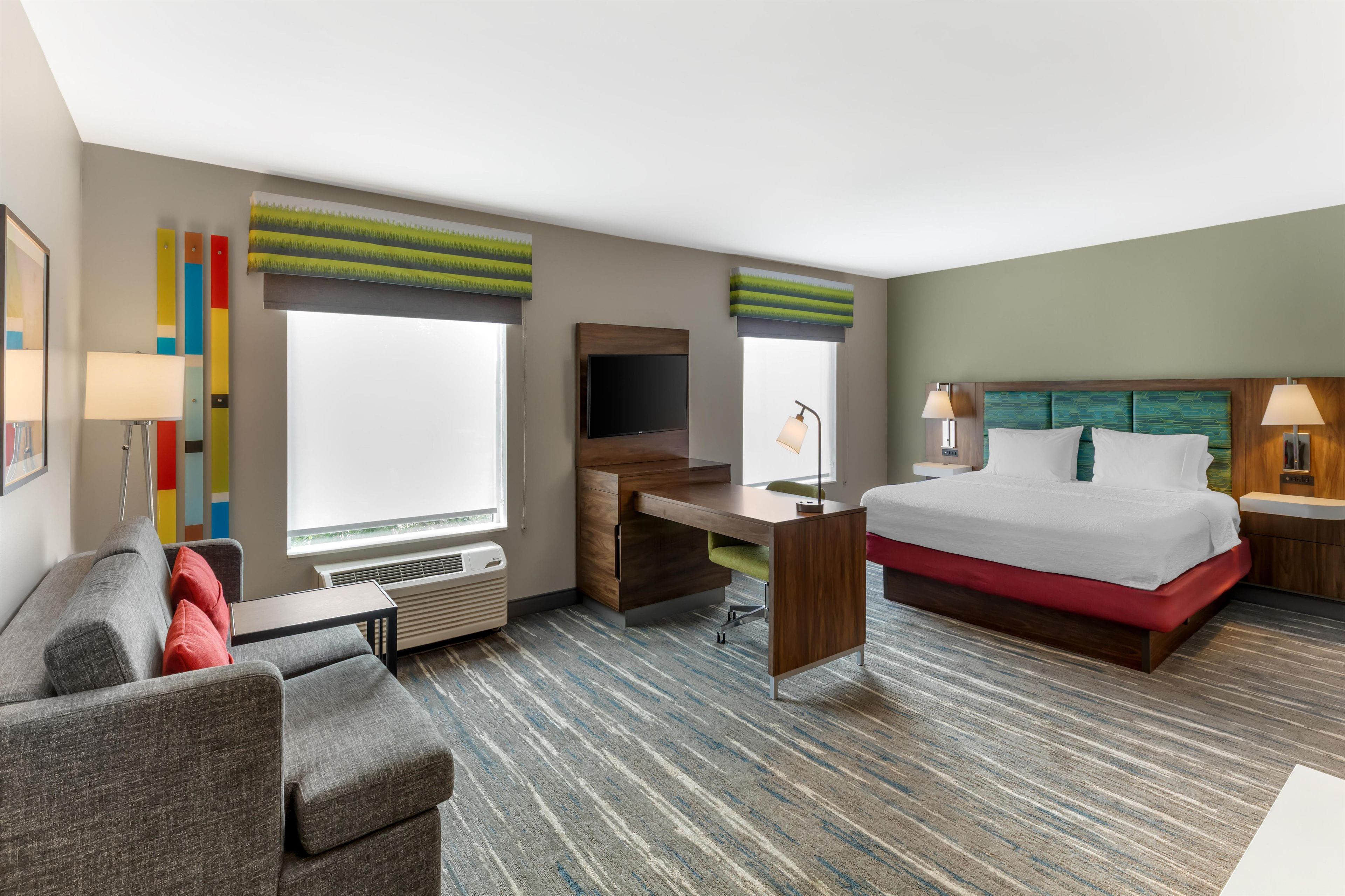 A hotel room with a bed, desk, chair, and a TV.