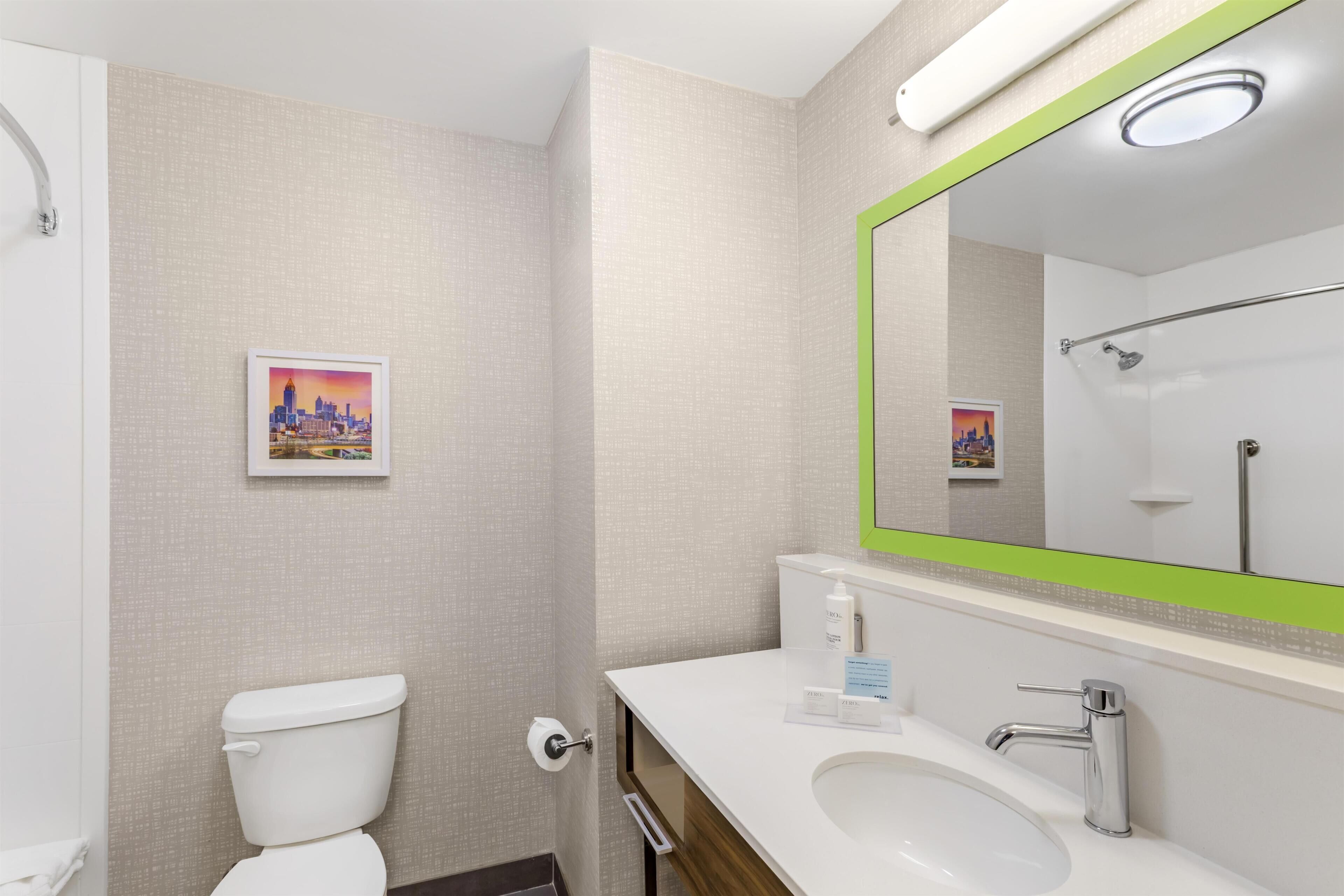 A modern bathroom with a toilet, sink, and shower. There are framed pictures on the wall.
