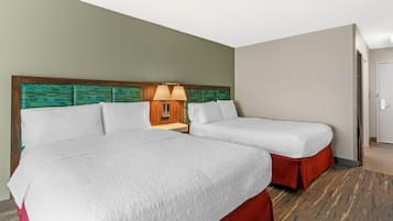 A hotel room with two beds, a nightstand with a lamp, and a door to the right.