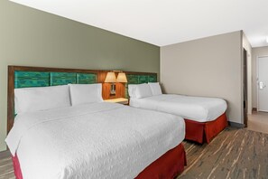 A hotel room with two beds, a nightstand with a lamp, and a door to the right.