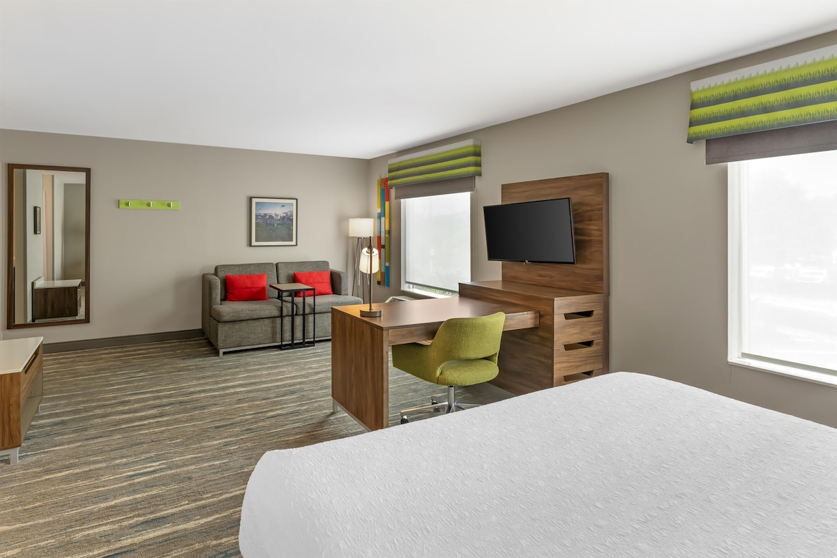 Una habitación de hotel con cama, escritorio, silla, televisor y ventana.