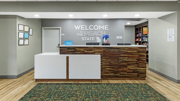 A reception desk with a 'WELCOME TO THE PEACH STATE' sign, framed certificates on the wall, and a 'Hilton Honors' sign.