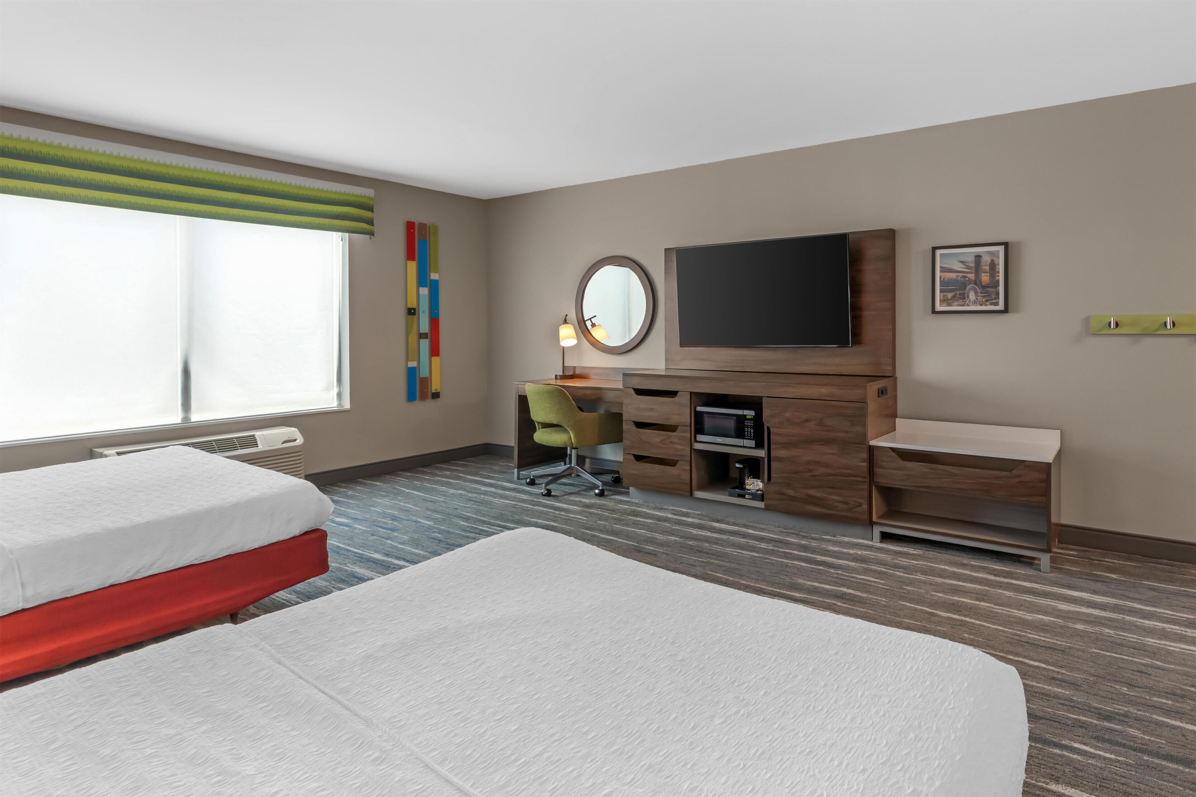 A hotel room with two beds, a desk, a television, and a window.
