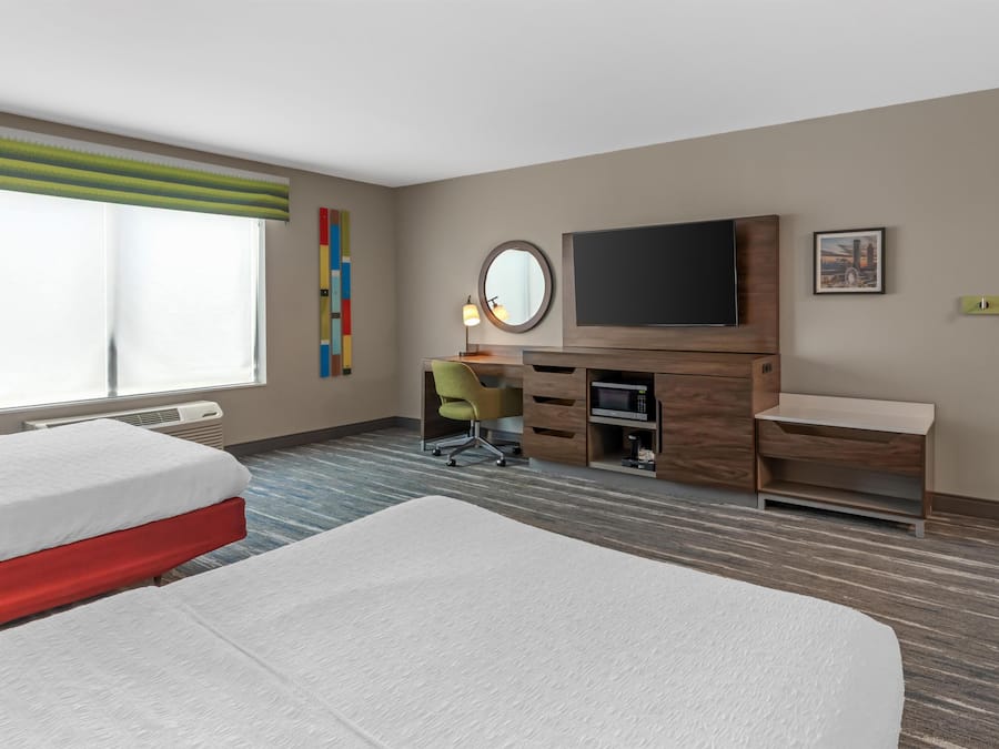 A hotel room with two beds, a desk, a television, and a window.